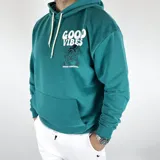 Canguro verde inglés de algodón peletizado, corte oversize, con capucha y cordones blancos. Estampa frontal y trasera con la frase "Good Vibes" y un personaje animado.