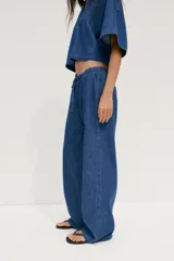 Pantalón de jean azul con cintura elástica ajustable con cordones, tiro medio y bolsillos de parche en la parte trasera.