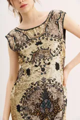 Vestido corto sin mangas, ajustado al cuerpo, con cuello redondo. Confeccionado en tela dorada con bordados y lentejuelas en tonos tierra y negro, formando un diseño ornamental.