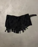 Short pollera negro de efecto gamuza o cuero sintético, con borde festoneado y tachas metálicas plateadas. Presenta flecos largos en el ruedo inferior y se ajusta con una hebilla en el lateral.