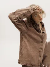 Camisa de denim color marrón gastado, con cuello camisero, corte holgado y cierre frontal con botones.