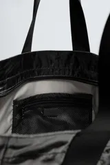 Bolso tipo shopper negro con acabado metalizado. Tiene un compartimento principal con cierre de cremallera y un bolsillo interior de malla con cremallera.