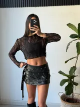 Minifalda negra de cuero sintético con tres tiras horizontales con ojales y hebillas plateadas.