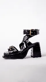 Sandalias de tacón negras con textura de piel de cocodrilo, plataforma cuadrada, tiras cruzadas y pulsera con hebilla dorada al tobillo.