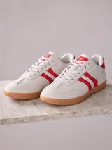 Championes urbanos color gris claro con detalles en rojo, suela color caramelo y logo de la marca en el lateral.