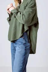 Camisa verde militar de manga larga con cuello camisero, cierre frontal con botones, dos bolsillos con solapa en el pecho y puños abotonados.