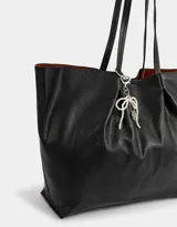 Cartera shopper negra de cuerina con manijas superiores y acceso mediante broche imantado. Incluye charm de perlas en forma de moño.