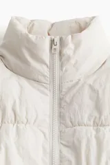 Chaleco puffer color crema con cuello alto, cierre frontal y bolsillos laterales invisibles.