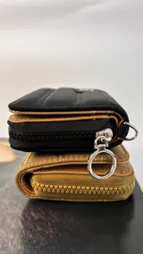 Billetera corta con cierre alrededor y tapa, confeccionada en tela capitoneada. Incluye varias reparticiones con tarjeteros y bolsillos internos, y una correa de mano desmontable. Disponible en negro, rojo y dorado.