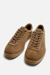 Zapatilla acordonada color marrón de piel serraje con pespuntes en el empeine y suela a tono.