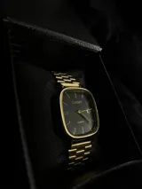 Reloj Casio Quartz dorado con caja cuadrada, dial negro y pulsera de eslabones.