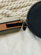 Monedero negro circular con cierre de cremallera y llavero de cinta estampada a rayas.