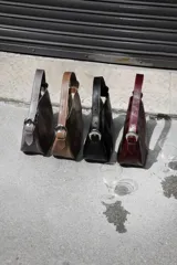 Cartera tipo lady bag color lila, de cuero sintético, con correa ajustable y herrajes metálicos plateados.