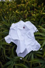 Remera blanca de manga corta con cuello redondo y estampado pequeño en el pecho de una figura humana caminando hacia una montaña.