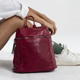 Mochila roja de símil cuero con apertura frontal y cierre metálico, detalle de grabado láser y costuras al frente, bolsillos internos, correas de galón regulables y asa de mano.