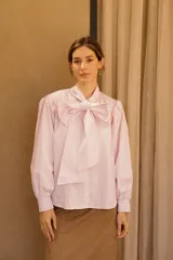 Camisa de algodón a rayas verticales rosas y blancas, con cuello alto y lazo grande en el cuello.