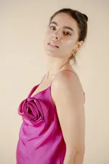 Vestido midi fucsia de satén con escote drapeado, breteles finos y tajo lateral. Presenta una rosa de tela en el bretel izquierdo.