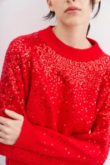 Sweater rojo de tejido de punto con cuello redondo y mangas largas. Diseño con lentejuelas rojas bordadas en el frente y las mangas.