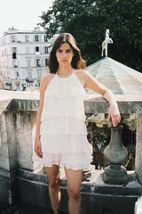 Minivestido blanco con cuello halter ajustable con lazos y falda escalonada con volantes. Espalda descubierta.