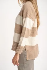 Sweater de punto con diseño de rayas horizontales anchas, alternando color beige camel y blanco roto con motas de color. Presenta cuello redondo y puños y borde inferior acanalados.