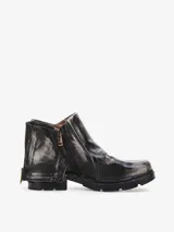 Bota corta de cuero bovino negro con efecto desgastado y envejecido, con detalles en gris claro. Presenta un diseño con solapa frontal que se ajusta con un broche y una cremallera lateral expuesta en el talón. Posee un taco bajo y cuadrado.