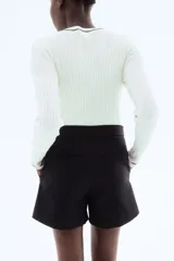 Short negro de tiro alto con cierre y pretina prolongada con botón. Modelo con bolsillos al bies y bolsillos insertados decorativos atrás.