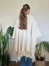 Ruana color crudo tejida a mano en punto arroz con lana merino. Presenta flecos en el borde inferior.