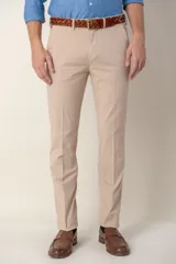 Pantalón de vestir color beige, de corte clásico, con bolsillos laterales y traseros. Se ajusta a la cintura con cinturón de cuero marrón trenzado.