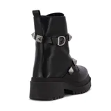 Bota de cuero sintético negra, de caña baja, con suela track y detalle de tachas piramidales plateadas en dos correas alrededor del tobillo.