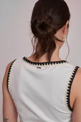 Remera negra ajustada al cuerpo, tipo musculosa, con escote redondo y ribetes en blanco con apliques de perlas en el contorno del cuello y las sisas.