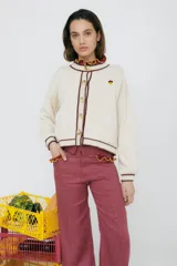 Cardigan color chocolate con cuello y borde de botones con detalle de crochet en color mostaza. Tiene un bordado de una bellota en el pecho.