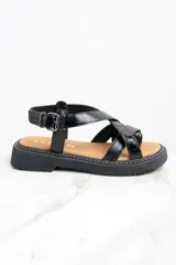 Sandalia de cuero color negro charol, con tiras cruzadas y hebilla ajustable al tobillo. Plataforma con suela track.