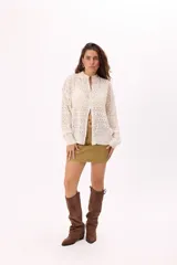 Cárdigan tejido calado color crudo con cierre frontal, cuello alto y mangas largas.