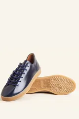 Zapatilla de cuero vacuno color azul marino, con cordones azules y suela de caucho color caramelo.