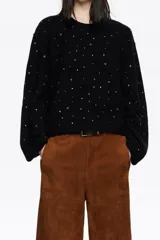 Sweater de punto negro confeccionado en mezcla de lana y alpaca. Presenta un diseño de corte recto con escote redondo, mangas largas tipo murciélago con maxipuños y detalles de piedras brillantes distribuidas por toda la prenda.