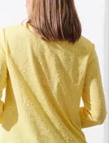 Blusa blanca de tejido labrado con cuello redondo, escote en V y aplique metálico.