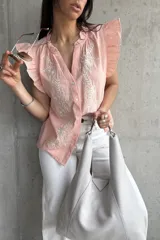Blusa color salmón con bordado de flores blancas, escote en V, mangas cortas con volados y cierre frontal con botones.