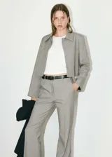 Chaqueta corta gris con cuello camisero, cierre frontal con botones ocultos, dos bolsillos de parche delanteros y forro interior.