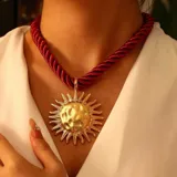 Collar con cordón trenzado color rojo y dije dorado con forma de sol.