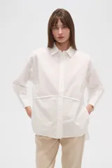 Camisa blanca de algodón, holgada, con cuello camisero, cierre frontal con botones y mangas largas.