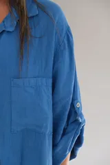 Camisola larga azul francia de lino italiano, con cuello camisero, mangas largas con puños abotonados, cierre frontal con botones y bolsillos de parche en el pecho.