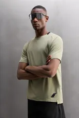 Camiseta deportiva verde militar confeccionada en tejido estructurado, ligero y elástico. Tiene cuello redondo, manga corta y bajo con aberturas laterales. Incluye logo estampado en el bajo.