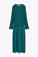 Vestido midi color verde esmeralda con textura plisada en la parte superior y falda lisa. Tiene cuello redondo y mangas largas.