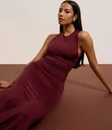 Vestido largo negro de microfibra, corte ajustado al cuerpo, con cuello redondo y escote tipo nadador en la espalda. Presenta una abertura lateral alta en la falda.