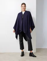 Ruana blanca de tejido suave, con ribete de eco cuero negro en los bordes y cierre frontal con botones metálicos dorados.