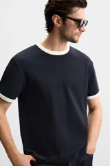 Camiseta azul marino de corte recto, con cuello redondo y mangas cortas. Presenta ribete blanco en cuello y mangas.