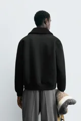 Cazadora negra de corte recto, confeccionada en tejido efecto ante con interior de borreguito sintético a tono. Presenta cuello de solapa, manga larga, bolsillos de vivo en la cadera, acabados en rib y cierre frontal con cremallera.