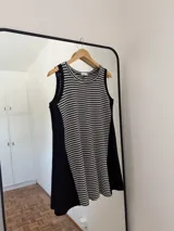 Vestido corto sin mangas, de silueta amplia y calce relajado. El frente es de tejido a rayas horizontales blancas y negras, mientras que los laterales son lisos en color negro. Posee escote redondo.