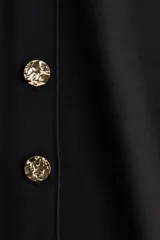 Chaleco negro de punto con cuello redondo y cierre frontal con botones dorados.