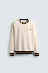 Sudadera color crema de corte regular fit, cuello redondo y manga larga. Presenta ribete a rayas en cuello, puños y bajo. Tiene un pequeño bordado de una flor en el pecho.